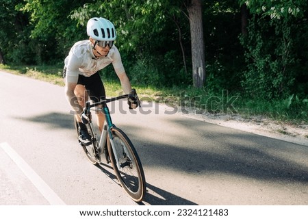 Photo of sportsman cyclist riding outside the city on a road bike in full gear against a forest background.