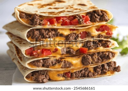 A photo of a stack of folded tortilla wraps filled with melted cheese, groundbeef, and diced tomatoes