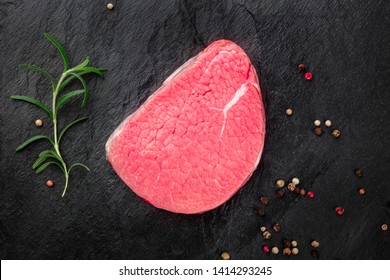 A Photo Of A Steak Of Eye Round Beef, A Raw Cut, With Rosemary And Peppercorns, Shot From The Top On A Black Background