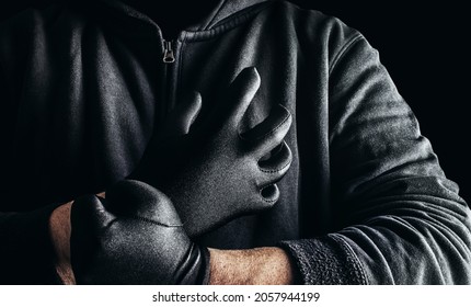 Photo of a stranger stalker man in black hood and clothing putting on gloves on dark background. - Powered by Shutterstock