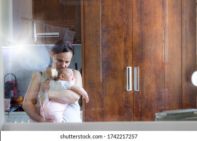 Photo Of Stressed Mother Holding Her Baby In Arms At Home.Tired Mom With Baby Girl In Her Arms Standing In The Kitchen.Shot Of A Mother And Her Baby Girl At Home.Sleepy Little Child With Mom. 