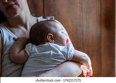 Photo Of Stressed Mother Holding Her Baby In Arms At Home.Tired Mom With Baby Girl In Her Arms Standing In The Kitchen.Shot Of A Mother And Her Baby Girl At Home.Sleepy Little Child With Mom. 