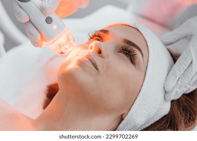 Photo from the studio of cosmetology, demonstrating the process of led therapy and facial skin care. A woman undergoes a procedure in a beauty salon. Beautician in white gloves use