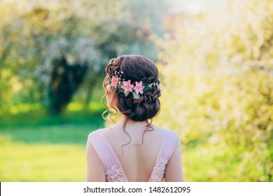 Photo of a stylish evening hairstyle for long hair, which are collected in an elegant bun with delicate, airy, curly locks. Wreath decoration with pink flowers and beads. Rear view - Powered by Shutterstock