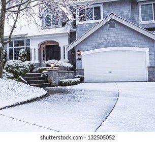 photo of suburban home with snow on drive way, lawn, plants, trees and roof