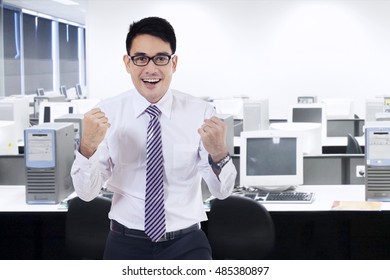 Photo of a successful worker celebrating his victory with arms up in the office room