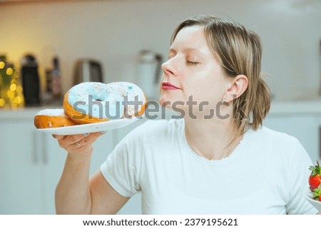 Photo of sugar addicted woman smells freshly baked donuts, impossible to resist eating dessert. Concept of dieting, resistance