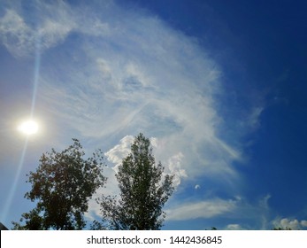 Photo Of Summer Blue Sky With Bright Sun, Cirrus Clouds And Trees In The Foreground And Sun Glare.