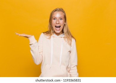 Photo Of Surprised School Girl With Dental Braces Holding Copyspace At Palm Isolated Over Yellow Background