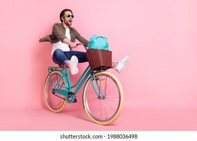 Photo Of Sweet Cute Guy Dressed Brown Shirt Dark Eyeglasses Riding Bike Backpack Looking Empty Space Isolated Pink Color Background