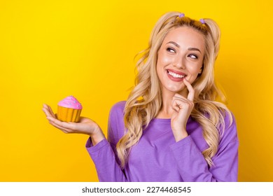 Photo of sweet dreamy lady dressed purple shirt rising cupcake finger mouth looking emtpy space isolated yellow color background - Powered by Shutterstock