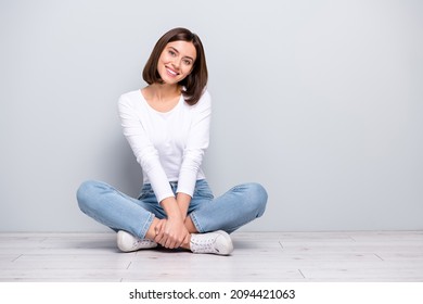 Photo of sweet dreamy young lady dressed white clothes smiling sitting legs crossed empty space isolated concrete grey wall background - Powered by Shutterstock