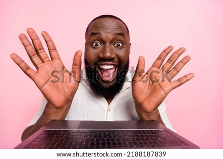 Photo of sweet excited young man wear white shirt typing modern device rising arms palms isolated pink color background