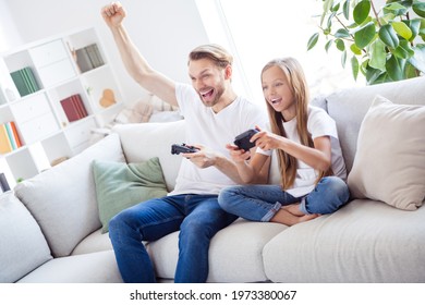 Photo of sweet funky father daughter dressed casual clothes sitting couch having playstation game competition indoors house apartment