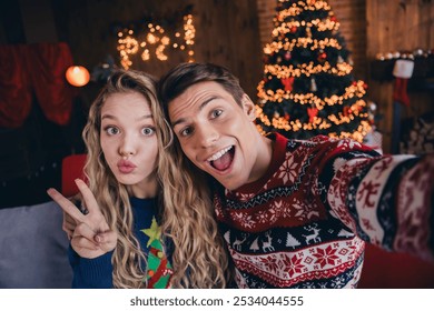 Photo of sweet good mood couple wear print sweaters tacking selfie showing v-sign sending kiss celebrating noel xmas indoors room home house - Powered by Shutterstock