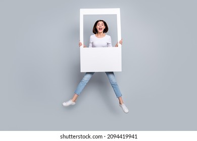 Photo of sweet impressed young woman wear white outfit jumping high holding white photo frame smiling isolated grey color background - Shutterstock ID 2094419941