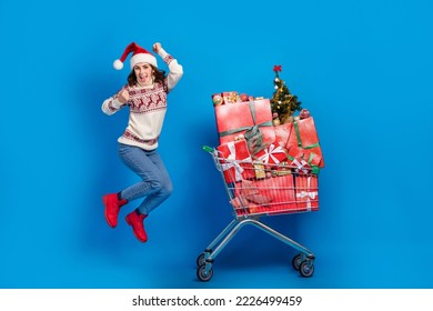 Photo of sweet lucky girl dressed print sweater claus cap running jumping choosing gifts supermarket tray isolated blue color background