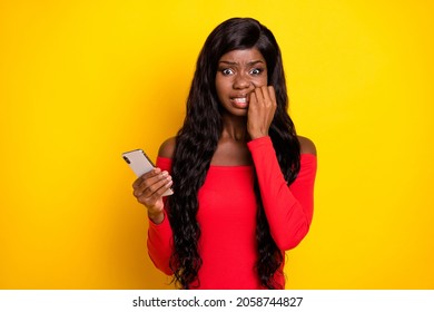 Photo Of Sweet Scared Dark Skin Lady Wear Off-shoulders Top Holding Modern Device Biting Fingers Isolated Yellow Color Background