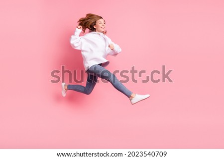 Photo of sweet shiny school girl wear white hoodie smiling jumping high running looking empty space isolated pink color background