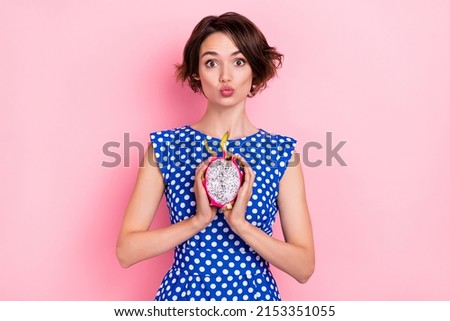 Photo of sweet young brunette lady hold dragon fruit blow kiss wear dotted blouse isolated on pink color background
