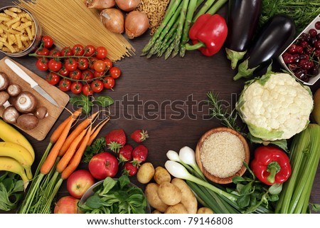 Photo of a table top full of fresh vegetables, fruit, and other healthy foods with a space in the middle for text.
