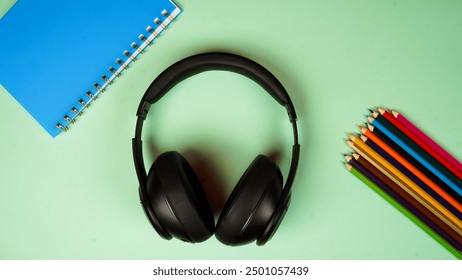 photo of table top view on green or turquoise background. with black wireless headphones, blue book, and colored pencils. - Powered by Shutterstock