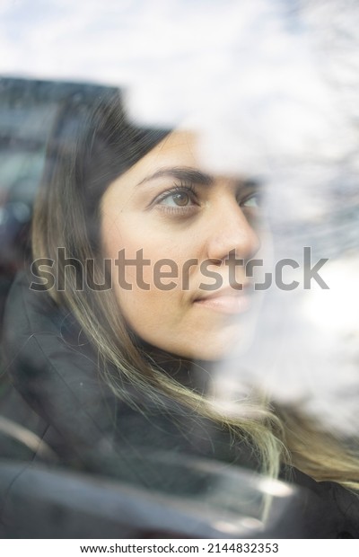 Photo taken from behind the car window. Young\
beautiful girl looks hopeful. Travel, break, and beginning new life\
concept.