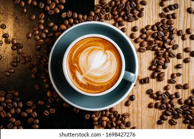 Photo Taken From The Top PointBlack Cup Of Coffee On The Black And Brown Table Among Spilled Roasted Coffee Beans. Cappuccino With Cofee Art In The Cafe.