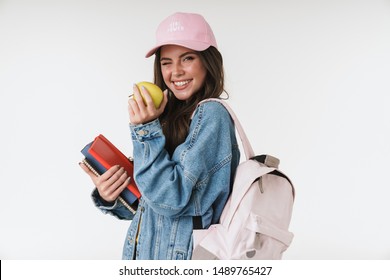 Photo Of Teenage Student Girl Wearing Cap Smiling While Holding Green Apple And Studying Books Isolated Over White Background