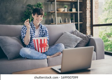 Photo Of Teenager School Boy Sitting Comfy Couch Stay Home Quarantine Watch Notebook Movie Online Show Eat Popcorn Good Mood Legs Crossed Living Room Indoors