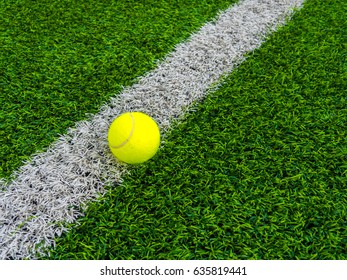 Photo of a tennis ball on a grass next to the white line