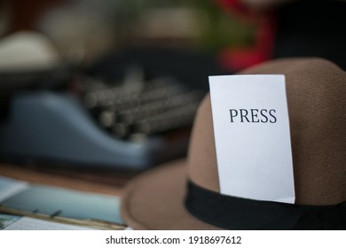 In The Photo There Is A Desk, A Typewriter And A Hat With A Press Badge