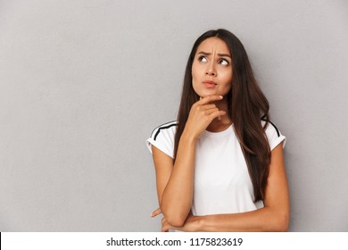 Photo of thinking young woman isolated over grey background looking aside.