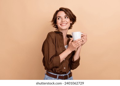 Photo of thoughtful dreamy girl dressed brown shirt enjoying tea looking back empty space isolated beige color background - Powered by Shutterstock