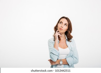 Photo of thoughtful young woman standing isolated over white wall background. Looking aside.