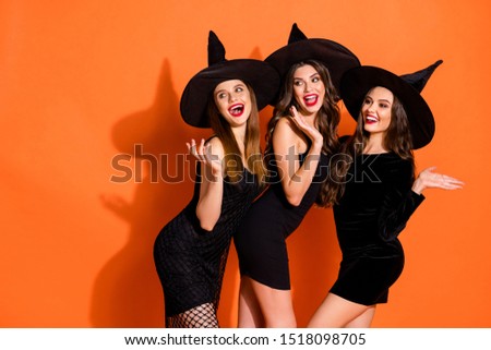 Photo of three cruel witch ladies calling handsome guys using magic powers wear short black dresses and wizard hats isolated orange color background