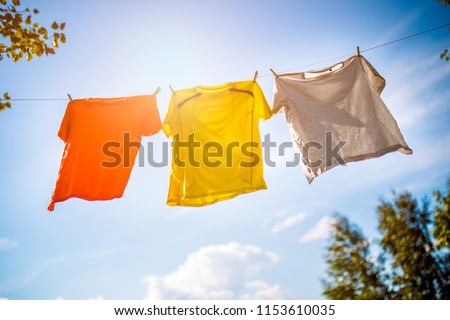 Photo of three T-shirts hanging on rope against blue sky background