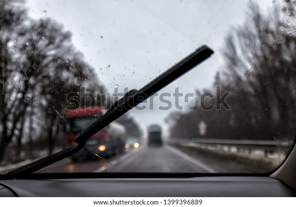 Photo through the windshield\
of the car in the raining evening, in the blur lights, track,\
trucks.