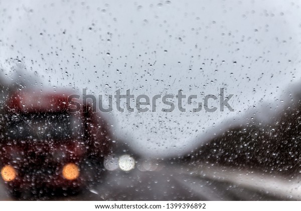 Photo through the windshield\
of the car in the raining evening, in the blur lights, track,\
trucks.