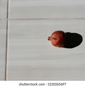 Photo Of Tiny Pomegranate Fruit On A Light Gray Tile Floor. Reflected Noon Sun