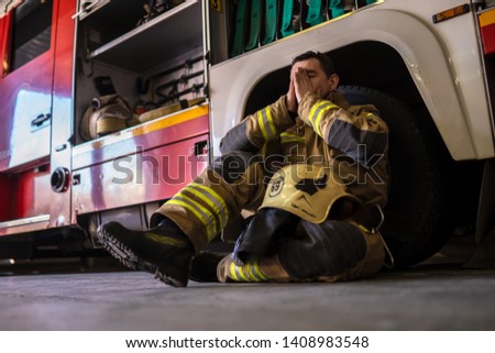 Photo of tired fireman sitting on floor near red fire truck