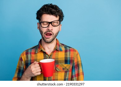 Photo of tired slumber man in eyeglasses wear checkered shirt yawn drink coffee trying to wake up isolated on blue color background