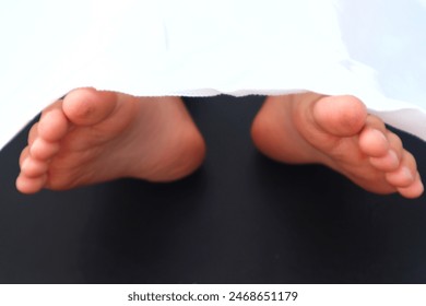 Photo of toddler's feet partially covered with white cloth with close view, dark background. - Powered by Shutterstock