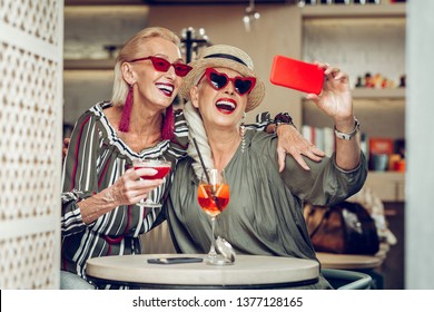 Photo together. Delighted senior women hugging each other while taking selfies together