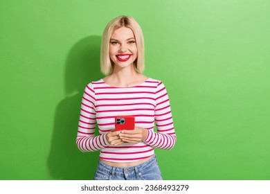 Photo of toothy beaming gorgeous girl with short hairdo dressed striped clothes holding smartphone isolated on green color background - Shutterstock ID 2368493279