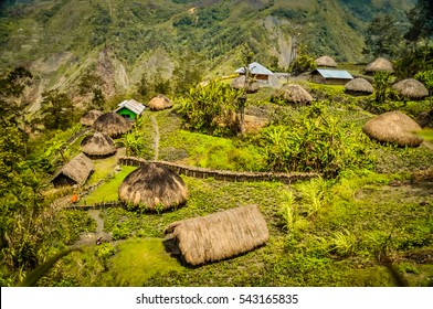 Photo of traditional village houses with straw roofs in village surrounded by high mountains in Dani circuit near Wamena, Papua, Indonesia.