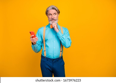 Photo Of Trendy Grandpa Hold Telephone Hands Look Empty Space Clever Person Arm On Chin Deep Thinking Wear Blue Shirt Suspenders Bow Tie Pants Isolated Yellow Color Background