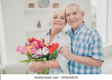 Photo of two adorable aged people hugging pair anniversary holiday surprise big red tulips bunch flat indoors - Powered by Shutterstock