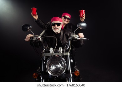 Photo Of Two Cool Old Bikers White Hair Man Lady Couple Drive Vintage Chopper Travel Festival Hold Plastic Beer Cups Celebrate Wear Rocker Leather Jacket Isolated Black Color Background