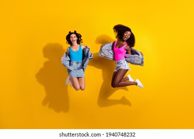 Photo of two crazy active ladies jump open mouth wear jeans shorts skirt jacket top shoes isolated yellow color background